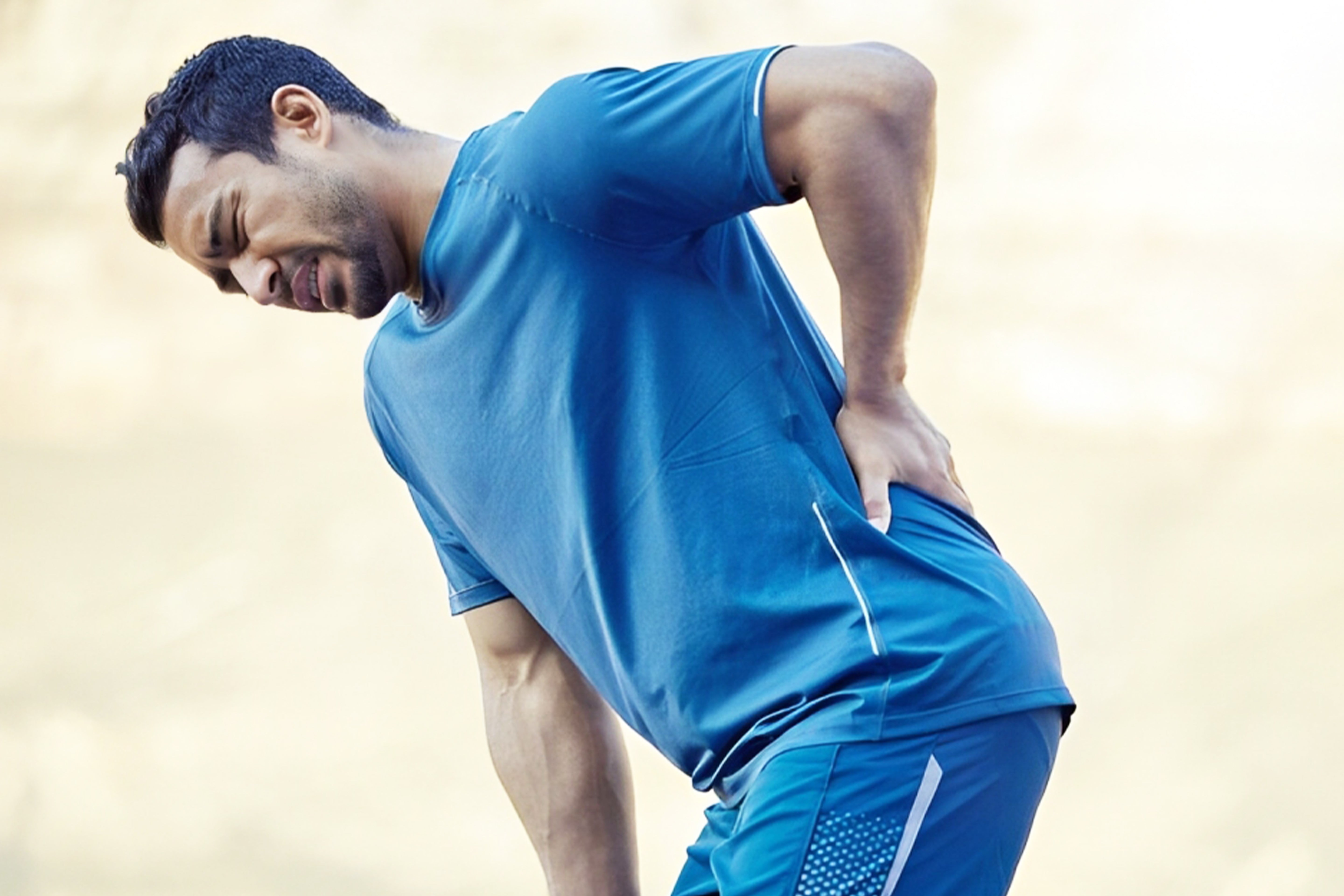 Athlete in blue activewear holding lower back in discomfort, possible muscle pain or injury